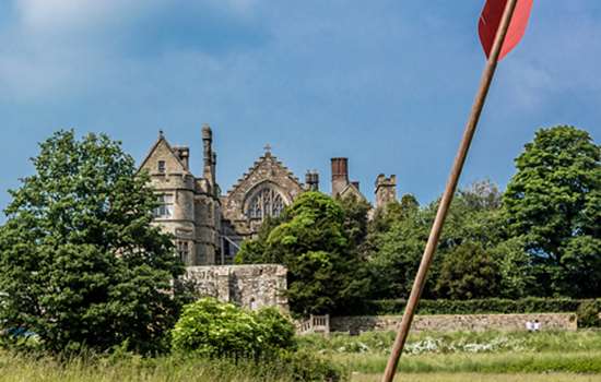 A red arrow positioned in a field, with view of Battle Abbey in the background.