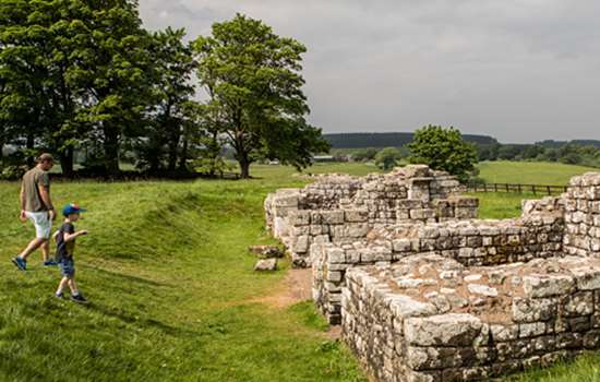 A view of stone wall ruins at Birdoswald Roman Fort with a man and a young boy walking towards them.