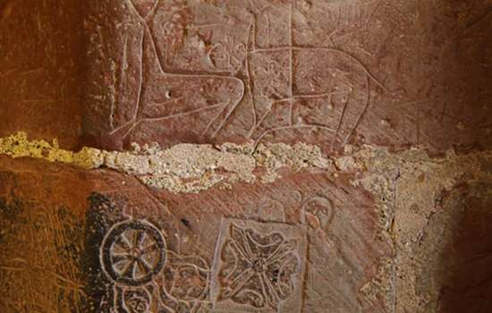 A close-up view of the stone walls at Carlisle Castle featuring historic graffiti, depicting images of deers and decorative flower symbols.