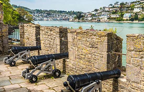 Cannons poke through battlements on a castle wall looking across a river estuary