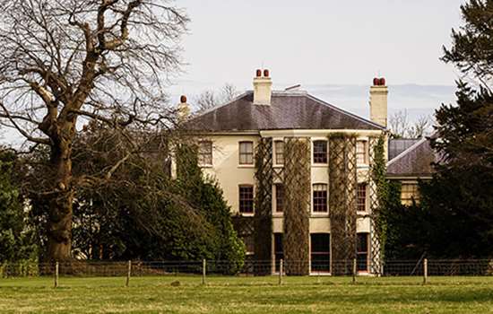 A grand house with ivy covered walls beyond a grass field