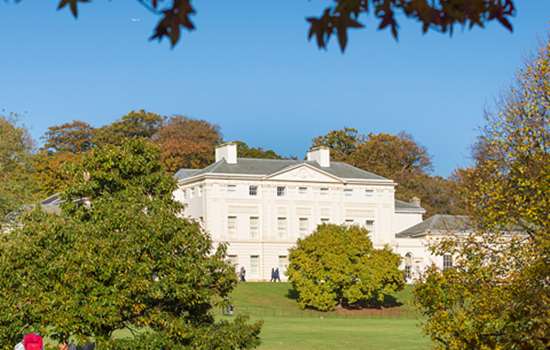 A view of Kenwood House through the trees, underneath a blue sky.