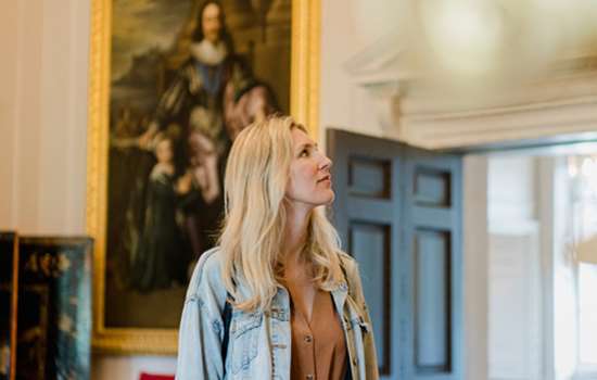 A woman wearing a denim jacket looks up in a room in Marble Hill House. There is a painting of Charles I on the wall behind.