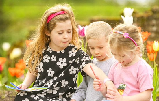 Three children sit on a wall looking at quest leaflet