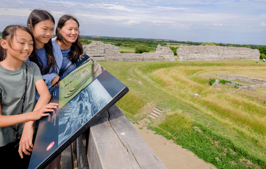 Photo of an adult and two children looking out over Richborough Roman Fort and Amphitheatre on a sunny day
